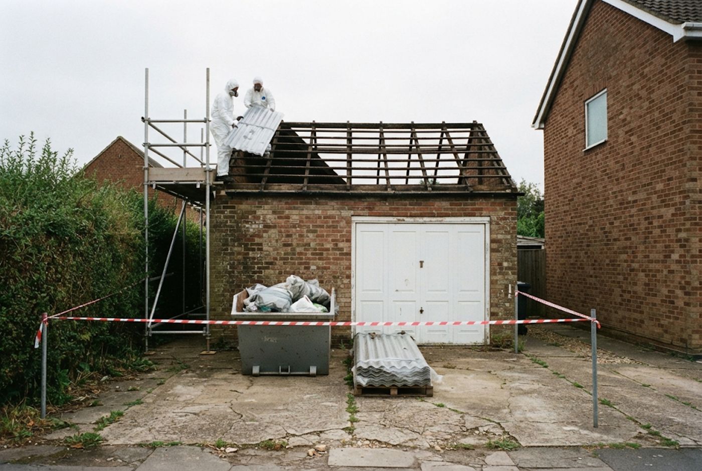 Garage roof removal in progress with waste skip and cordon